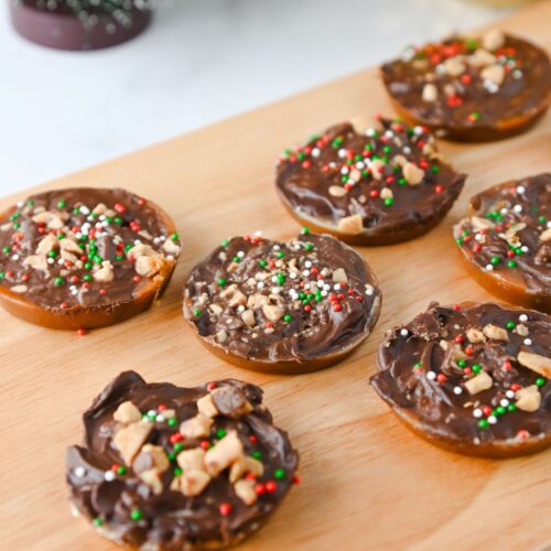Multiple Christmas crack cookies topped with chocolate, toffee, and sprinkles, all on a wooden cutting board.