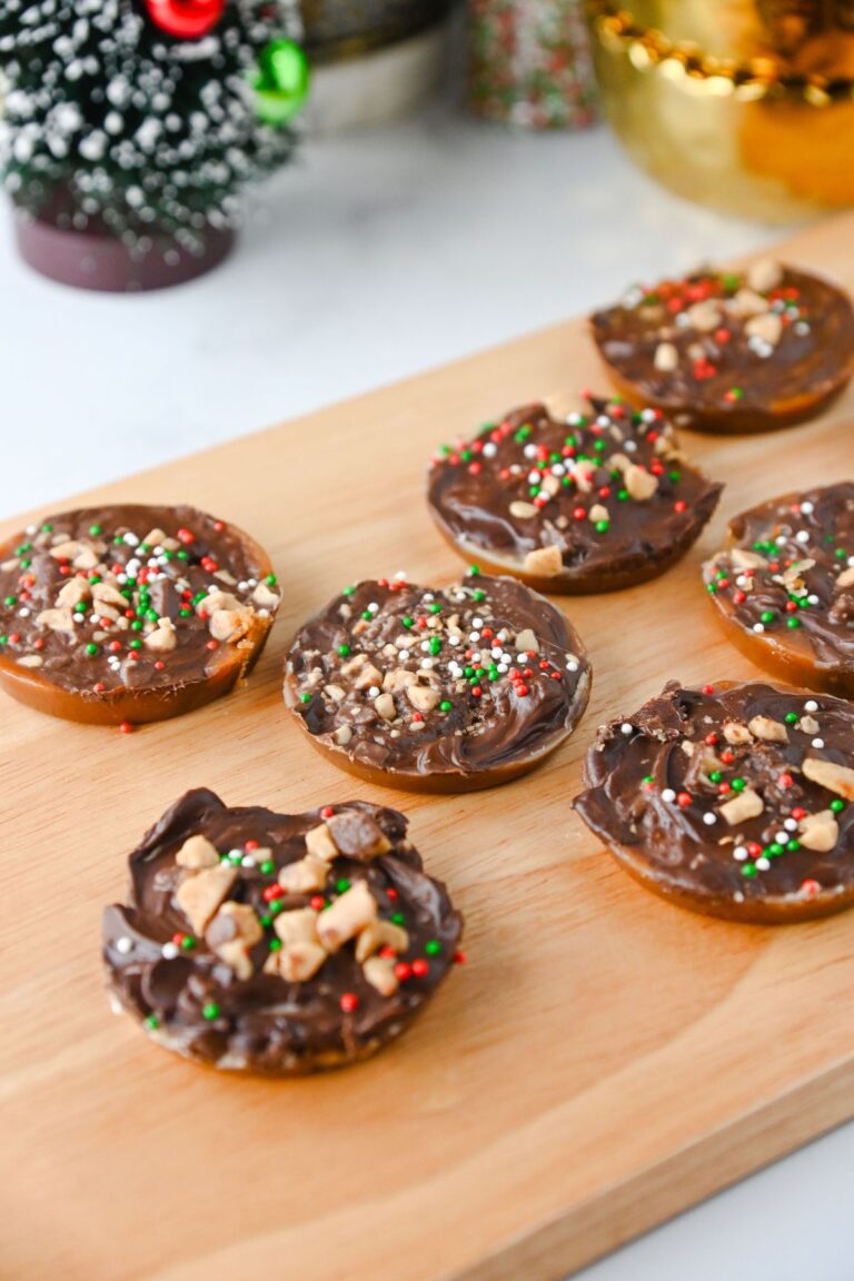 Multiple Christmas crack cookies topped with chocolate, toffee, and sprinkles, all on a wooden cutting board.
