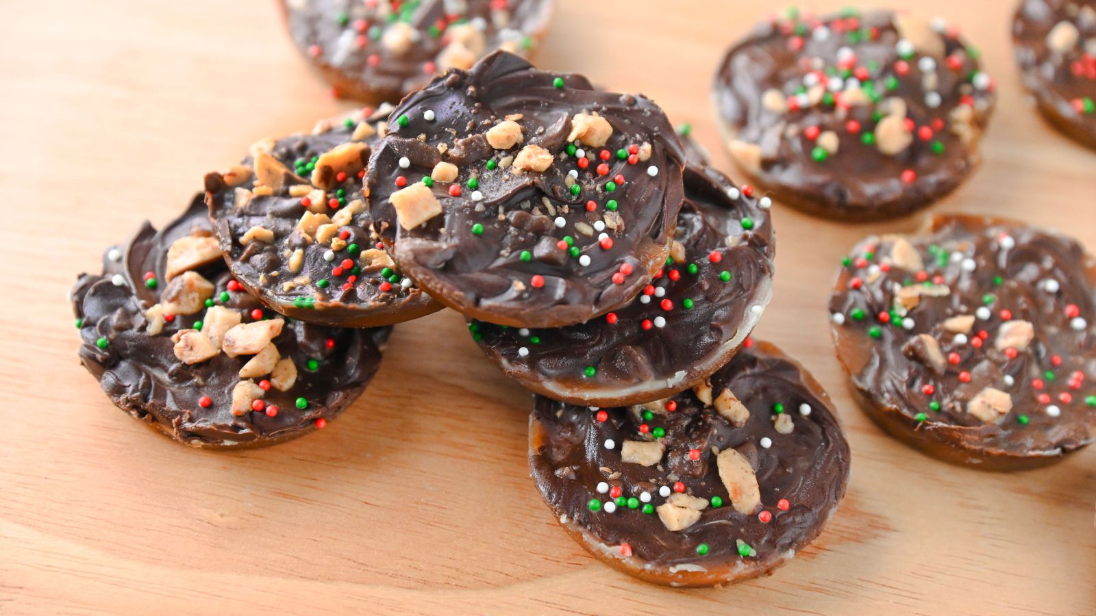 Multiple Christmas crack cookies topped with chocolate, toffee, and sprinkles stacked and placed on a cutting board.